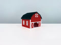 Red Barn miniature with white trim, a black roof and an open front doorway, shown from an angle.