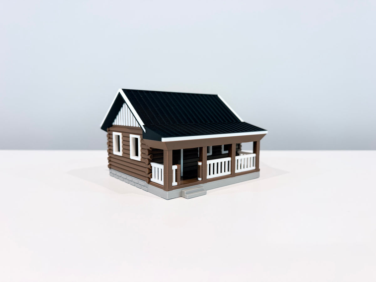 Brown log-style miniature cabin with a black roof, white porch railing and gray steps, shown from an angle.