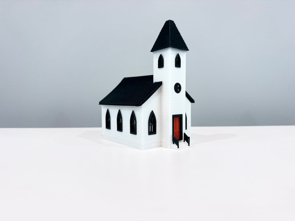 White Church miniature with a black spire, arched windows and a red entrance door, shown from an angle.