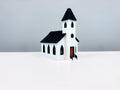 White Church miniature with a black spire, arched windows and a red entrance door, shown from an angle.