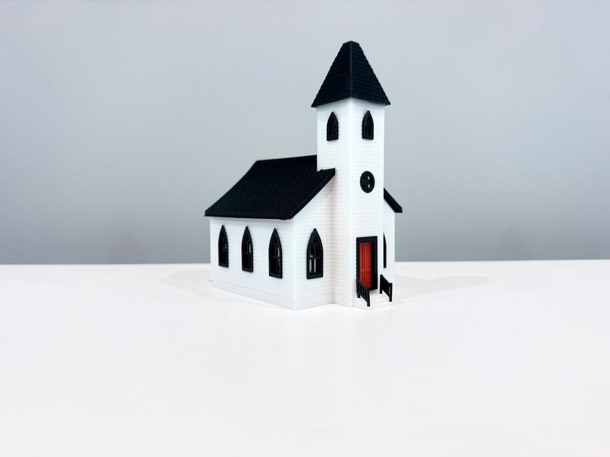 White Church miniature with a black spire, arched windows and a red entrance door, shown from an angle.