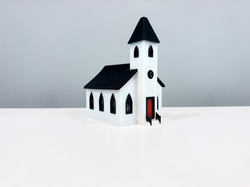 White Church miniature with a black spire, arched windows and a red entrance door, shown from an angle.