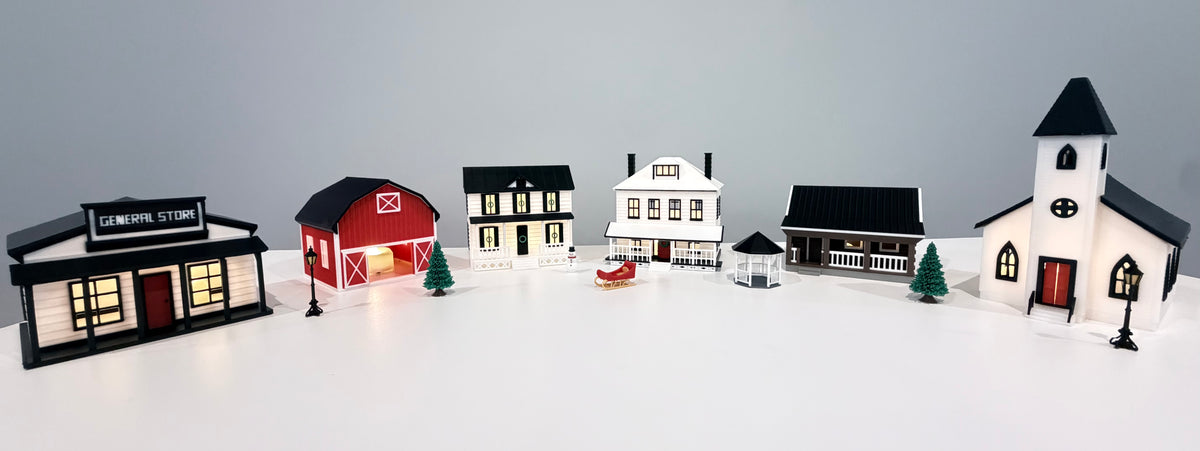 Primrose Christmas Village buildings and accessories arranged together on a white surface in daylight.