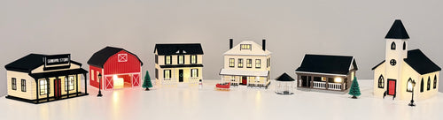 Primrose Christmas Village buildings and accessories arranged together with warm window lighting.