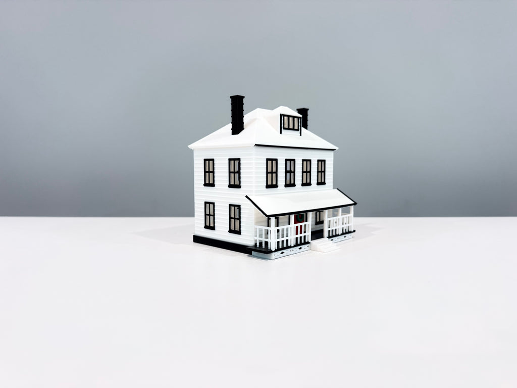 White Farmhouse miniature with a wide porch, white roof and two black chimneys, shown from an angle.