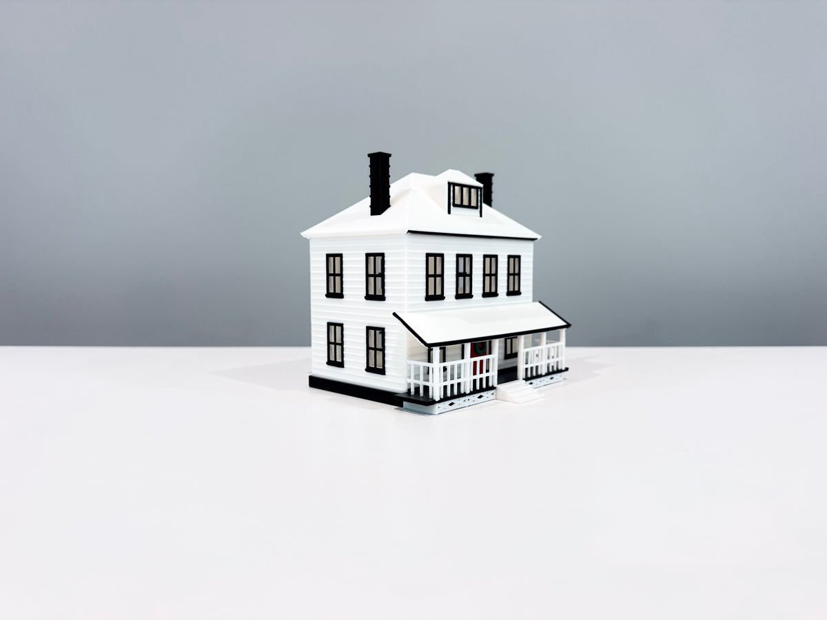 White Farmhouse miniature with a wide porch, white roof and two black chimneys, shown from an angle.