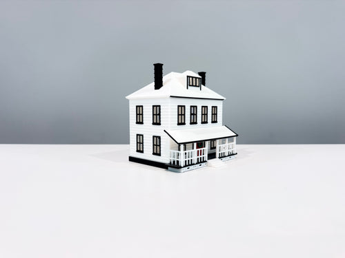 White Farmhouse miniature with a wide porch, white roof and two black chimneys, shown from an angle.