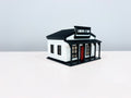 General Store miniature with white walls, black trim, a red door and a storefront sign, shown from an angle.