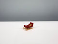 Red miniature sleigh with gold-colored runners on a white surface.