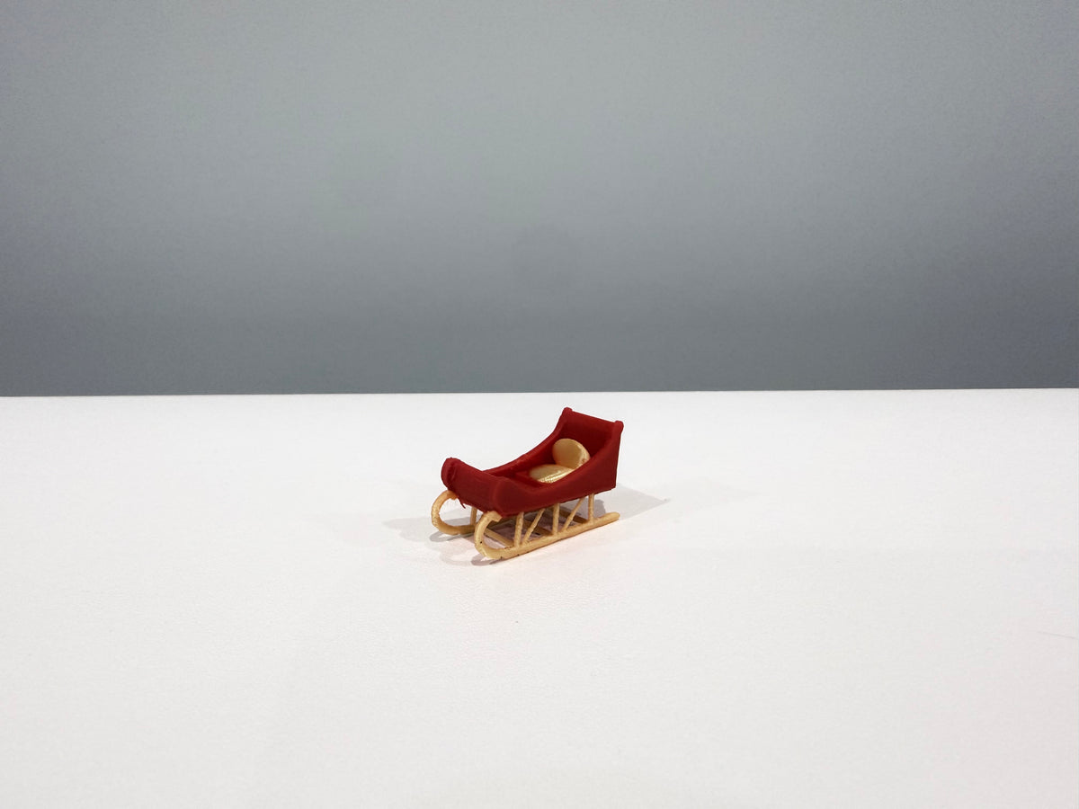 Red miniature sleigh with gold-colored runners on a white surface.