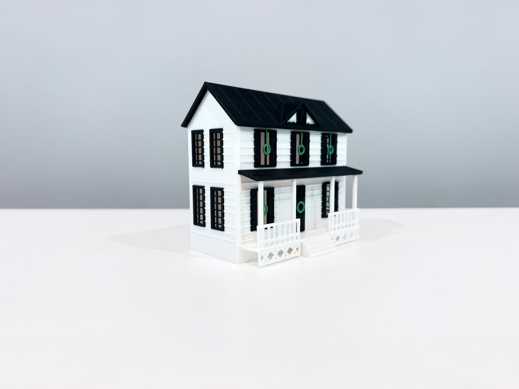 White two-story Village House miniature with a black gable roof, dormer and front porch, shown from an angle.