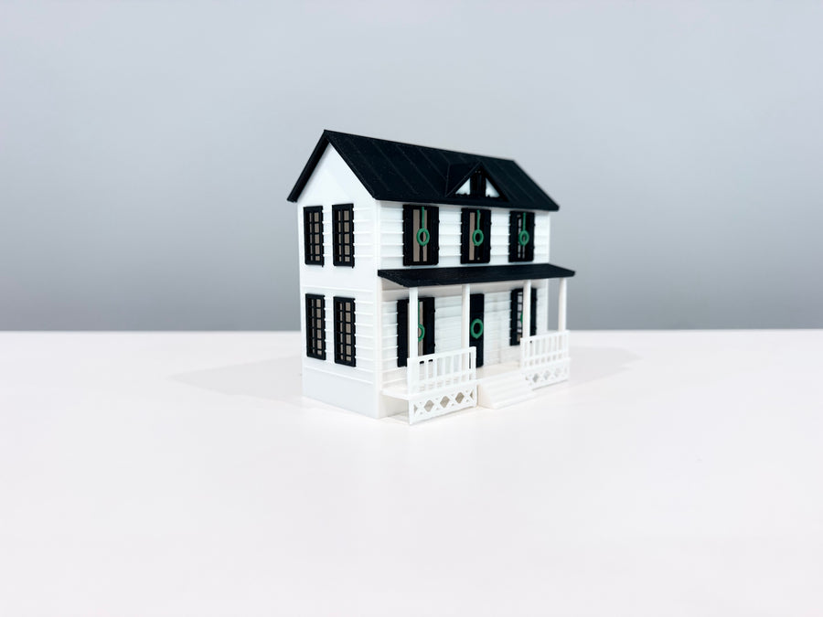 White two-story Village House miniature with a black gable roof, dormer and front porch, shown from an angle.