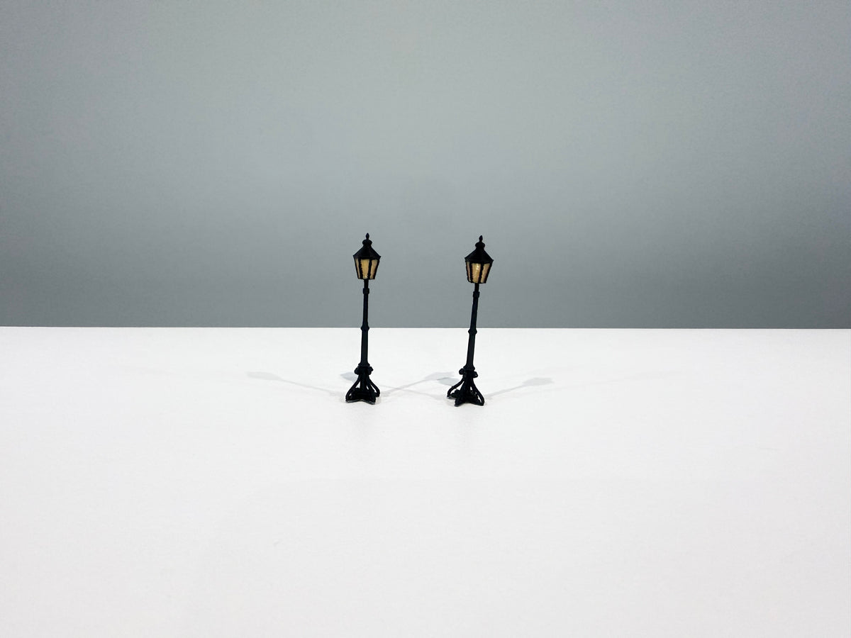Two black miniature light posts with warm-colored lantern panels.