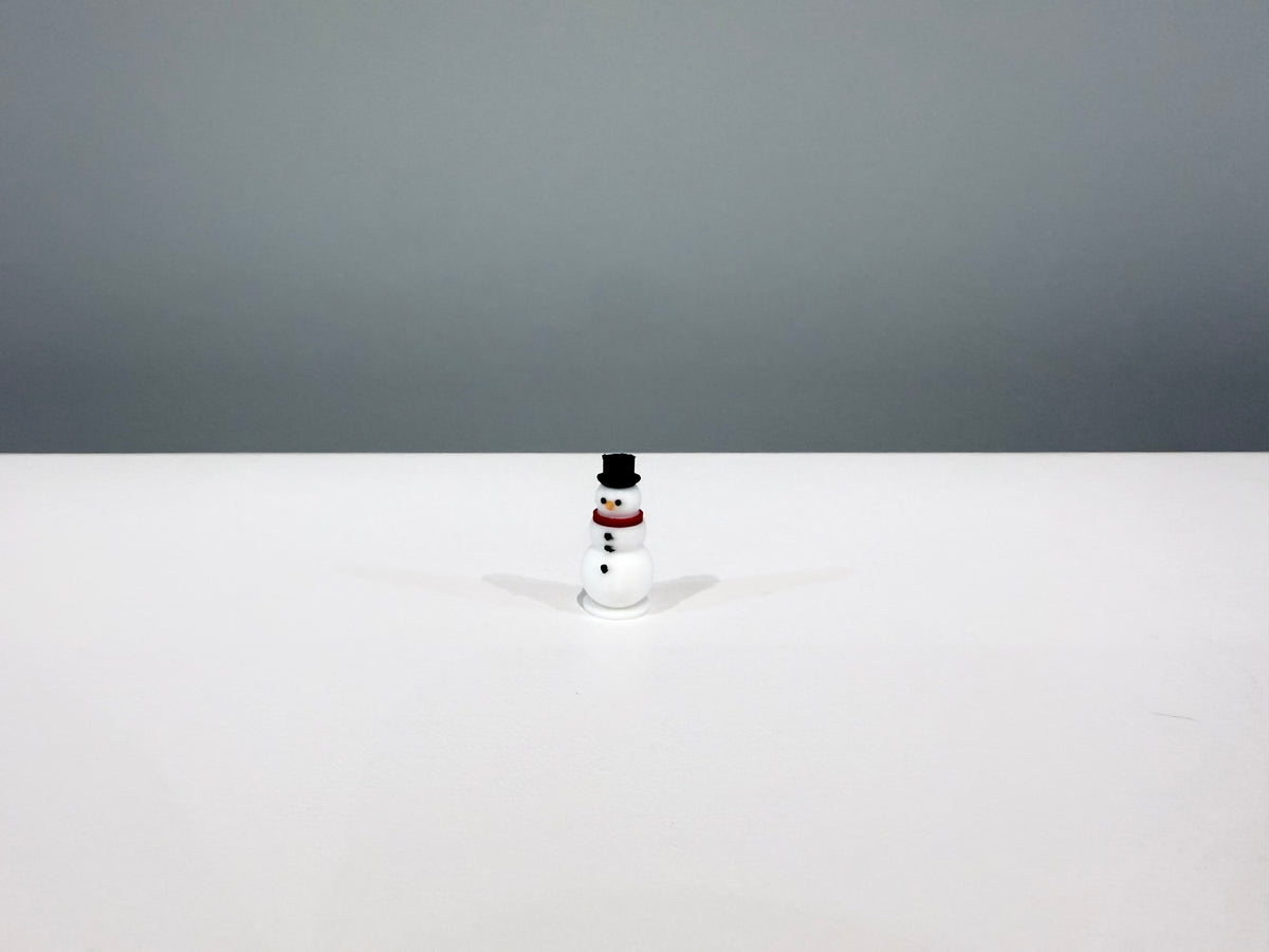 White miniature snowman wearing a black top hat and red scarf.